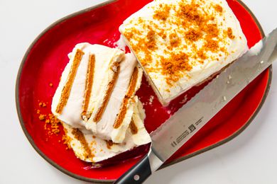 A biscoff ice cream cake served on a red plate, partially sliced with a knife visible