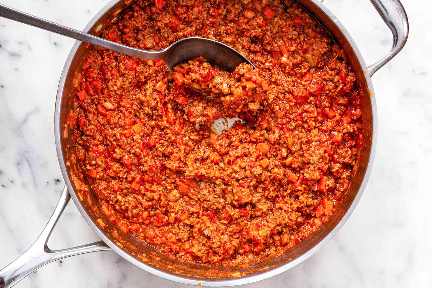 Scooping bolognese sauce out of a skillet.