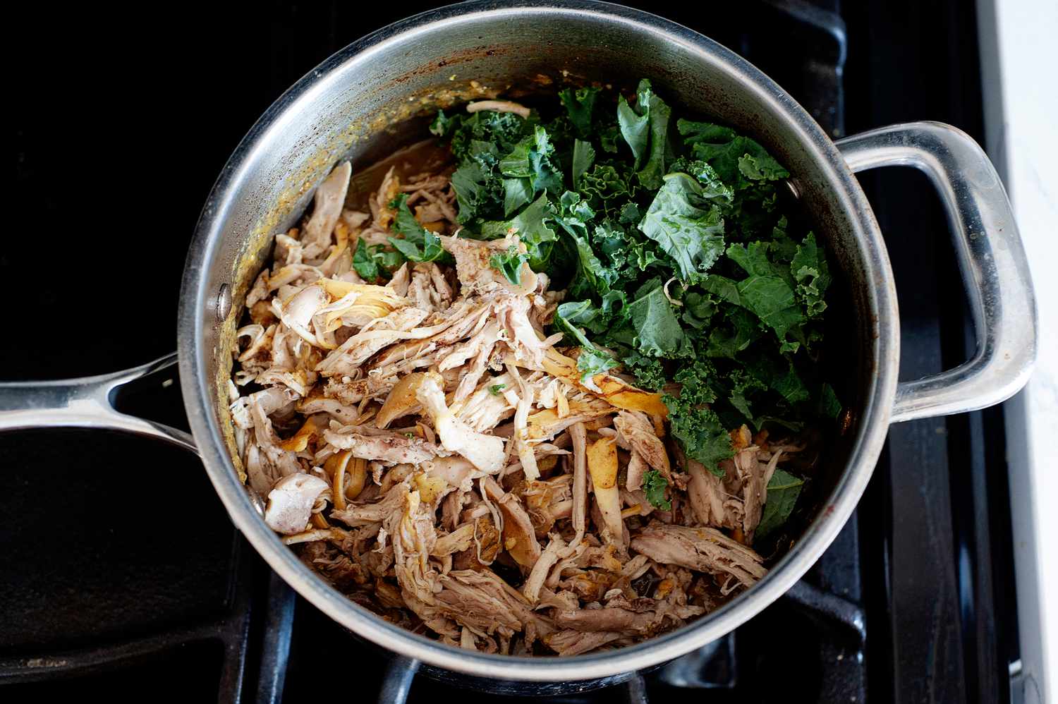 Shredded chicken and herbs in a pot on the stove to make “Ripe Figs” lemon chicken soup.