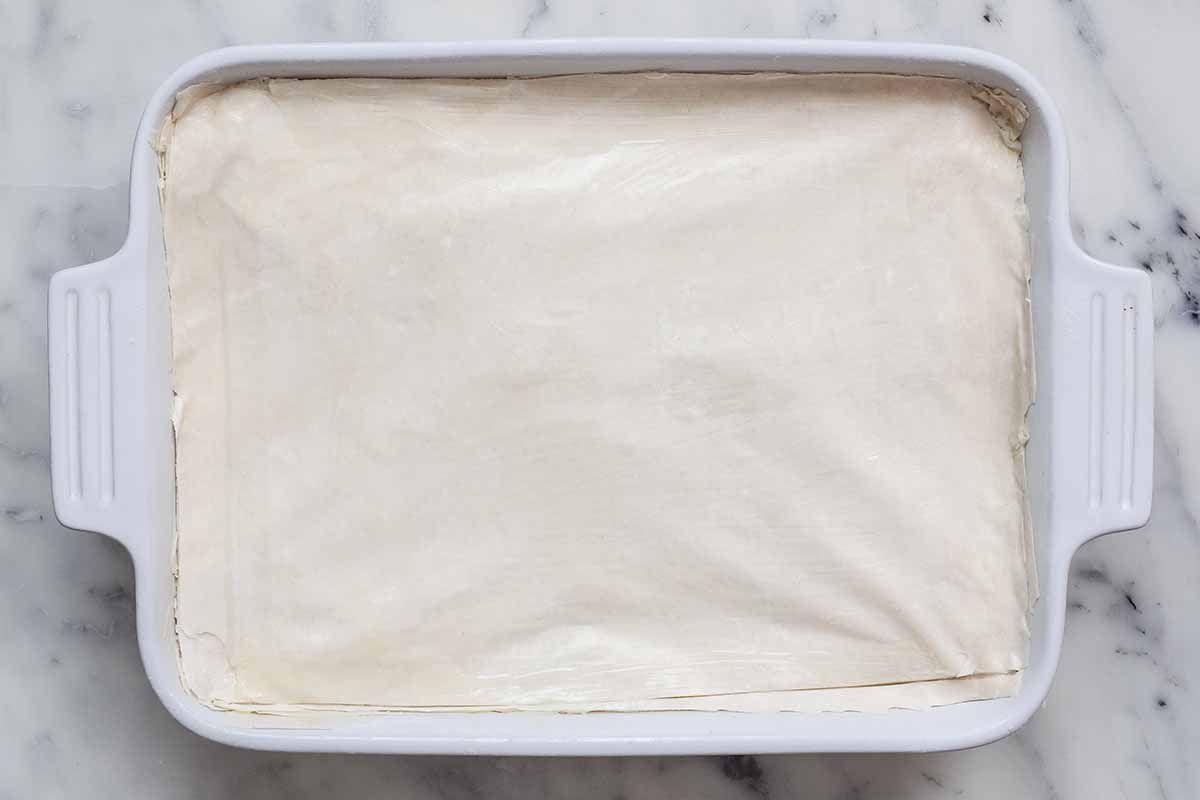 Phyllo covering the top of of a casserole dish filled with spinach and cheese for spanakopita.