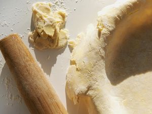 Pie crust being prepared next to dough and a rolling pin