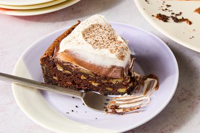 Closeup of a small multicolored plate with a slice of Mississippi Mud Pie with a fork next to a plate of the pie with several slices removed and a stack of empty plates
