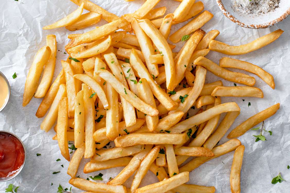 A serving of French fries on parchment paper garnished with parsley and accompanied by dipping sauces