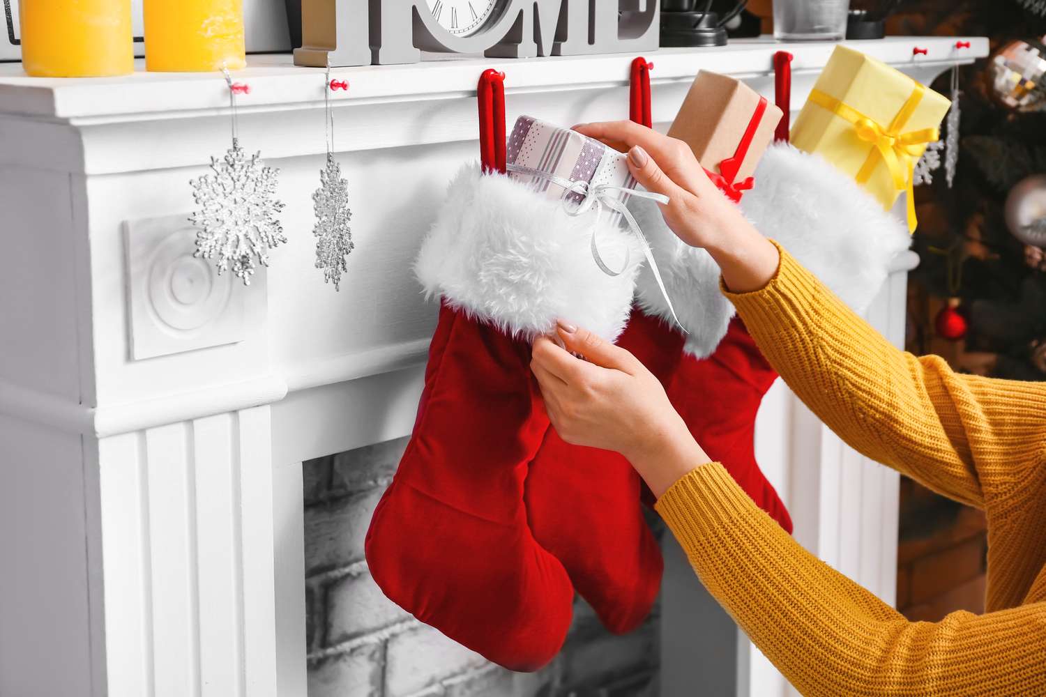A person placing gifts into red stockings hanging from a mantel