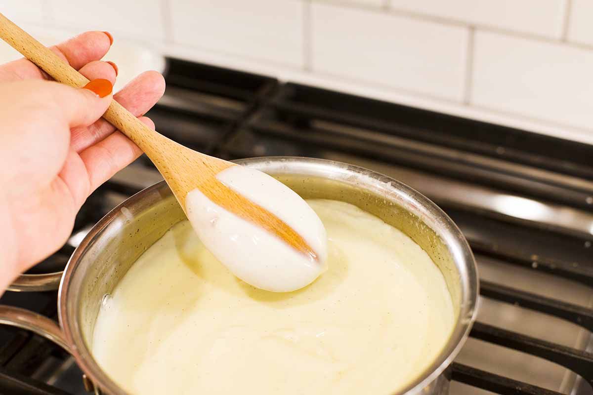 Photograph of vanilla pudding cooking on the stovetop. A wooden spoon is lifted out and a line is drawn through it to show the thickness of the pudding.