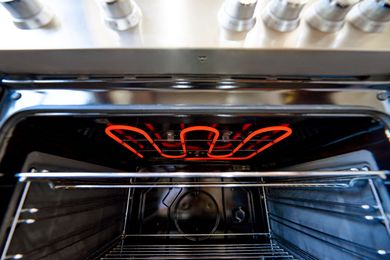 An oven interior with the broiler element glowing red on the top and oven racks visible inside