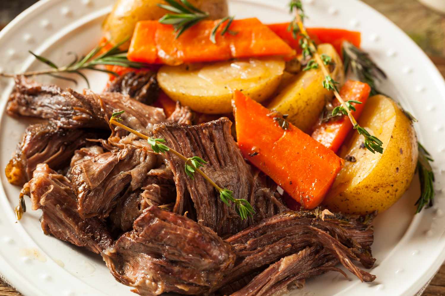 A plate of pot roast accompanied by roasted carrots and potatoes garnished with fresh herbs