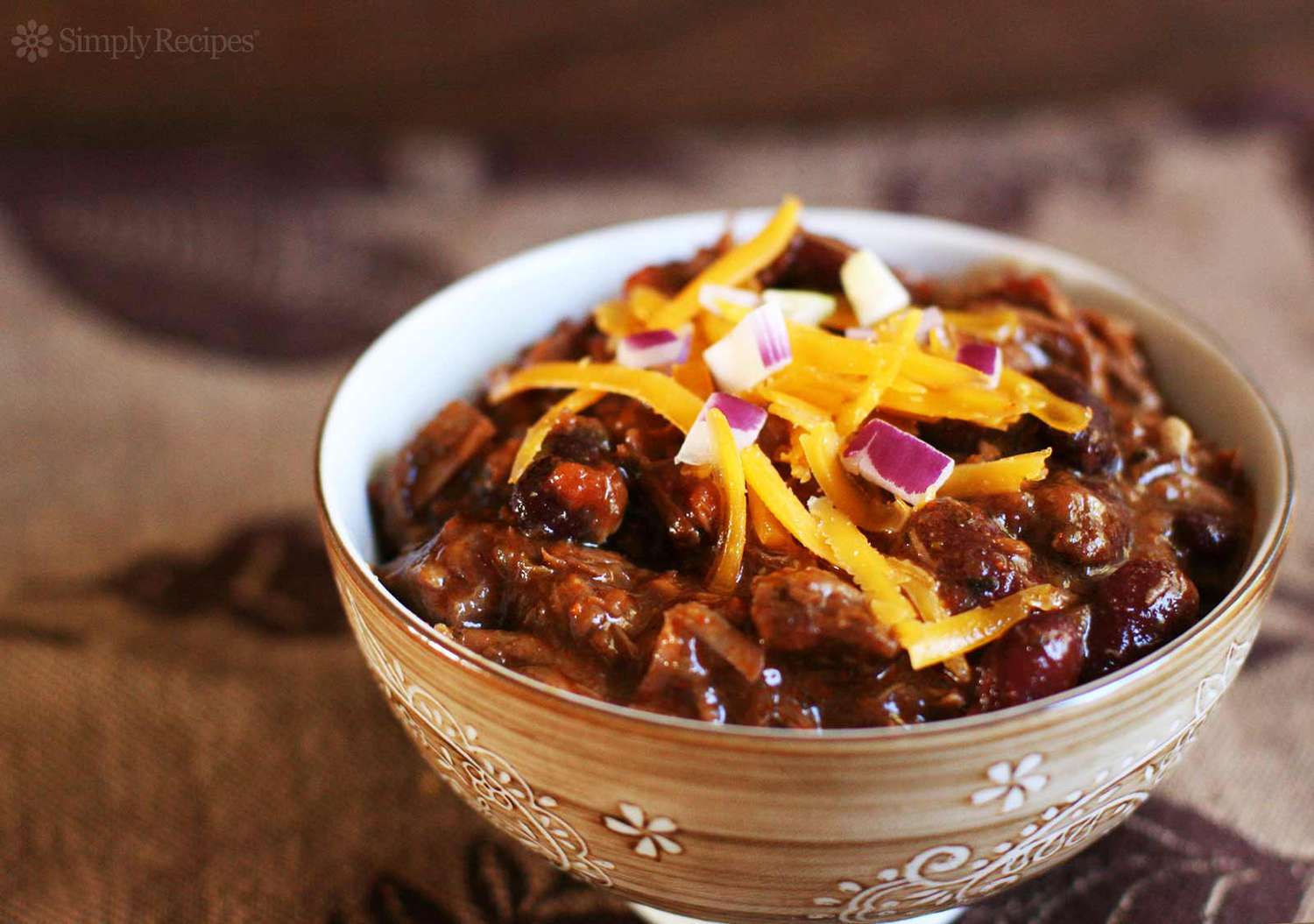 chili con carne topped with cheddar and red onion in a brown bowl