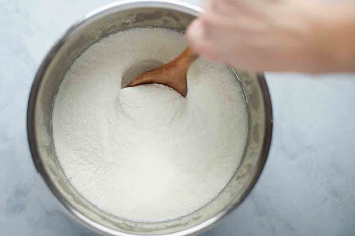 A wooden spoon checking the consistency of the yogurt in a pressure cooker