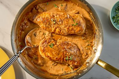 Two cooked chicken breasts in a creamy sauce in a skillet garnished with herbs