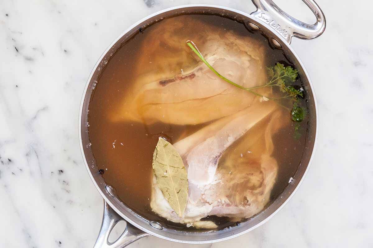 Chicken poaching in the water with a bay leaf to make easy chicken noodle casserole.