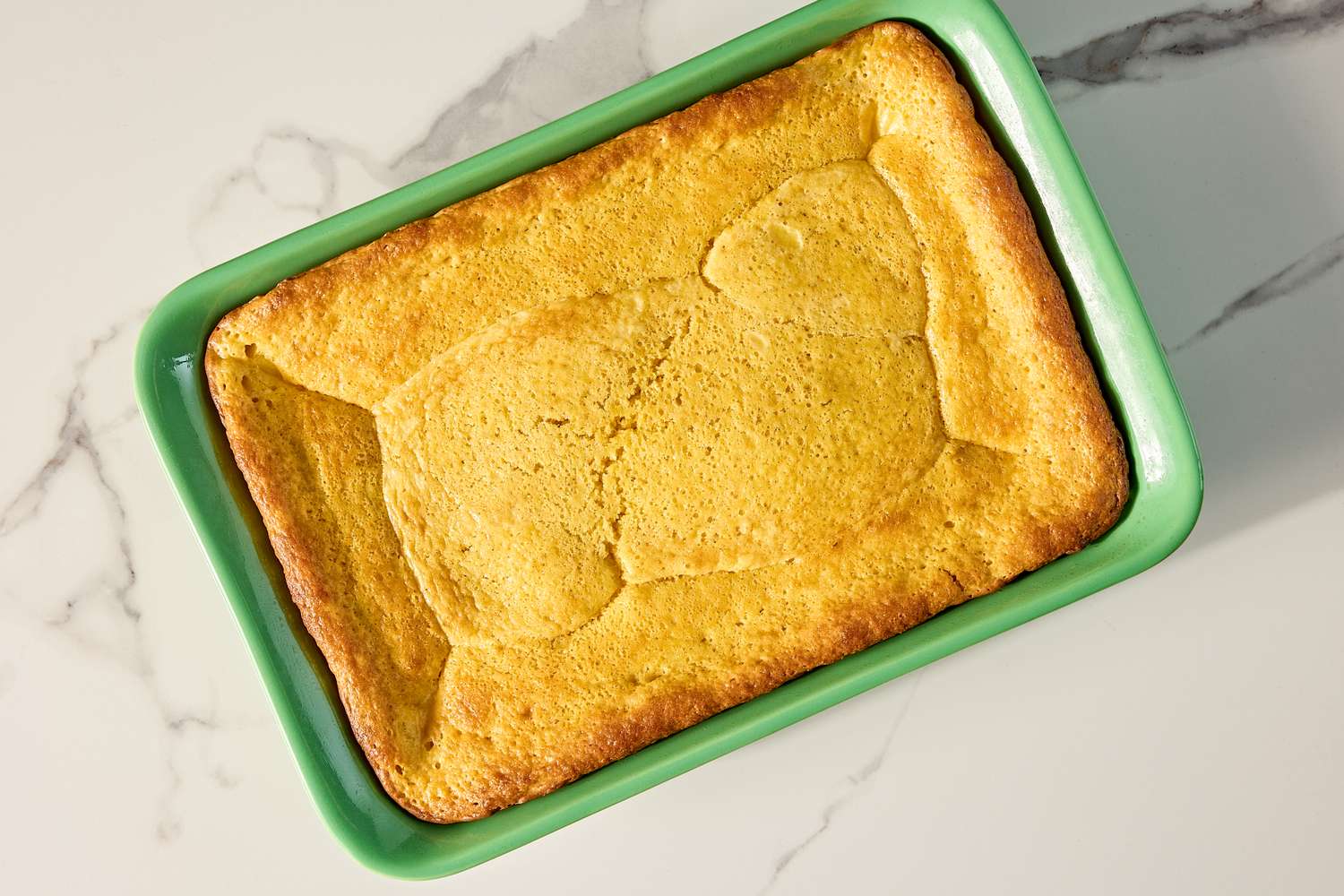 Freshly baked cake for the ugly cake recipe in a green baking dish on a marble countertop