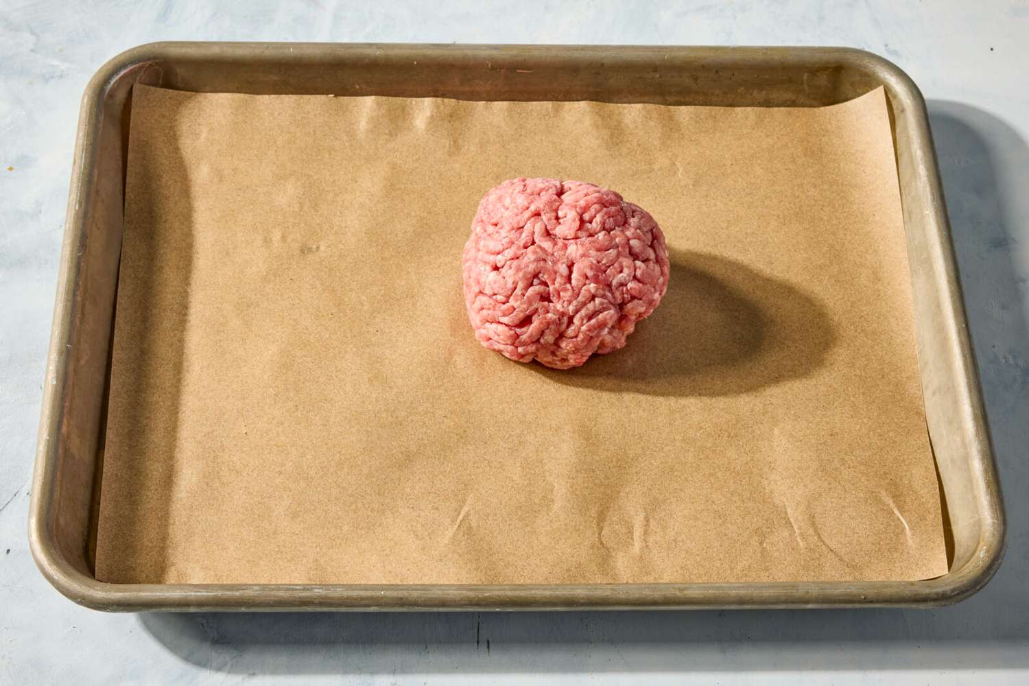 Ball of ground beef on a parchment-lined baking sheet