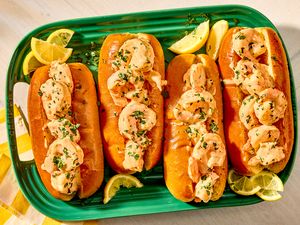 Four shrimp rolls on a green platter with lemon wedges and garnishes