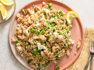 Plated asparagus and brown rice dish with beans and garnishes on a light surface with cutlery and a lemon wedge nearby