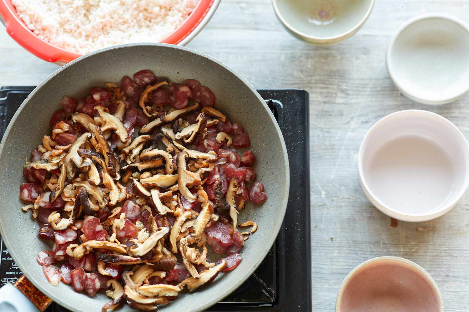 Mushrooms, dried pork, and shallots in a skillet to make steamed rice with sausage, dried shrimp, and mushrooms