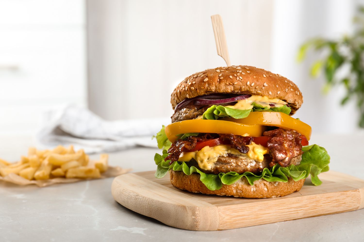 A loaded cheeseburger with vegetables and a bun on a wooden tray
