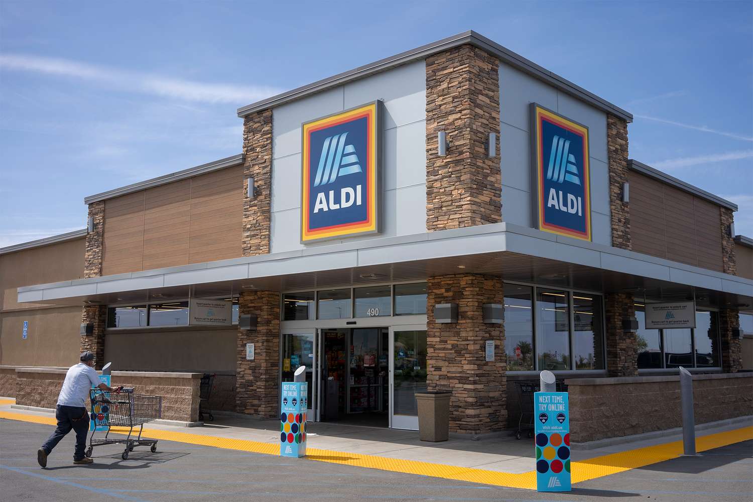 An Aldi grocery store exterior and a shopper pushing a cart in the parking lot