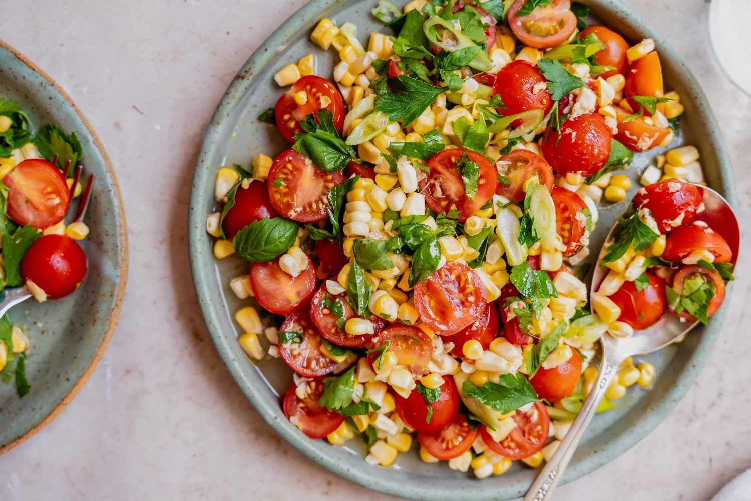 A plate of corn and tomato salad with fresh greens and a spoon