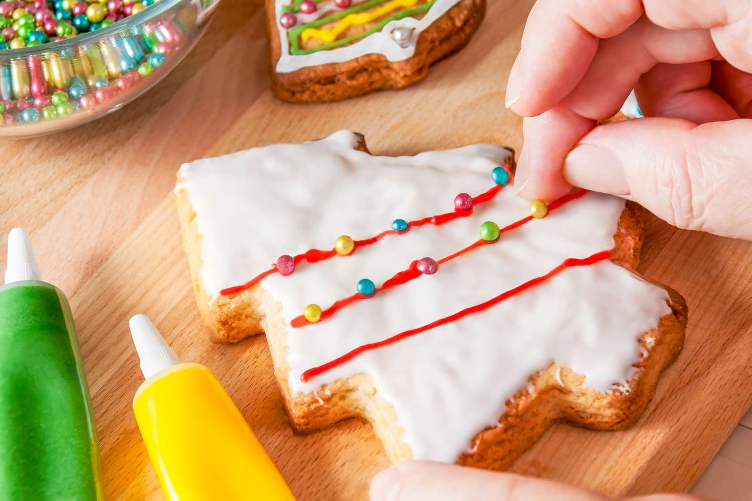 Someone decorating a christmas cookie with nonpareil sprinkles