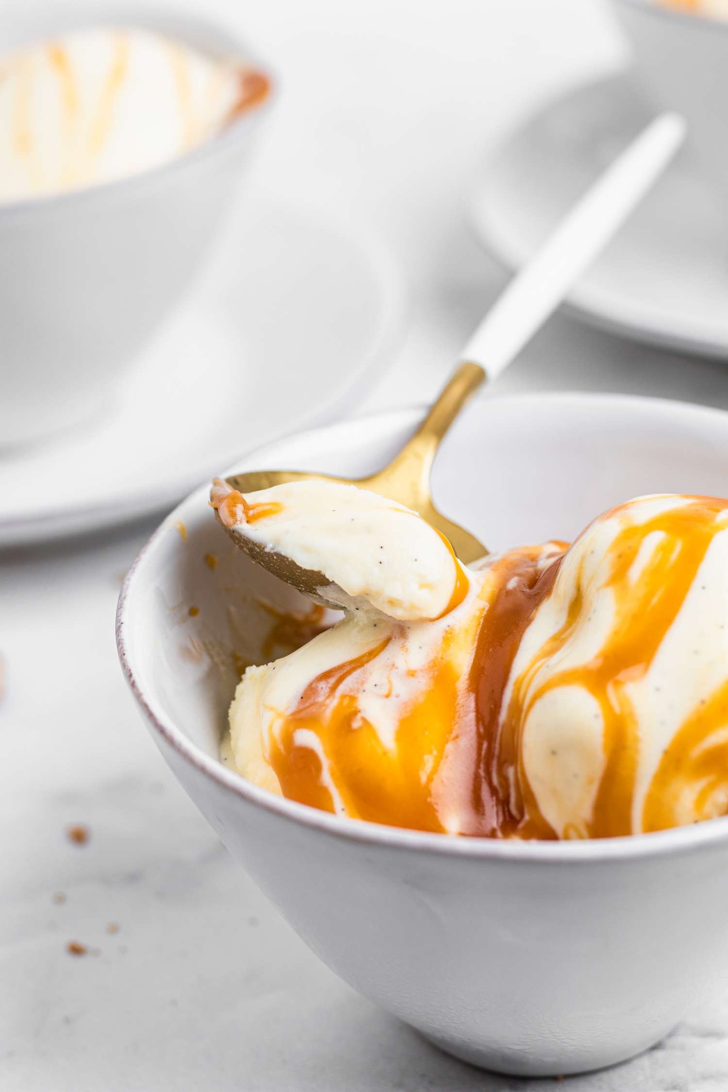 Side view of homemade vanilla ice cream topped with caramel and with a spoon.