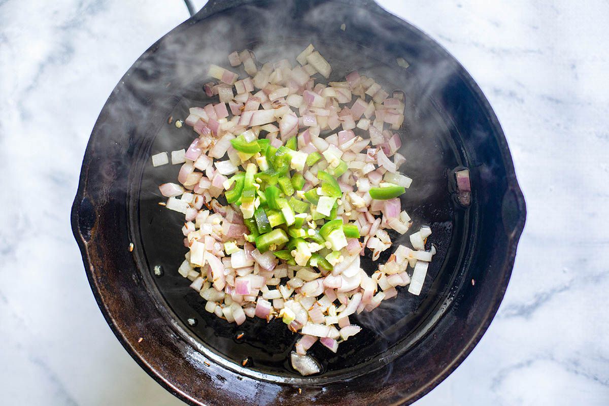 Onions, spices and jalapenos being toasted in a black skillet for vegetable samosa filling.