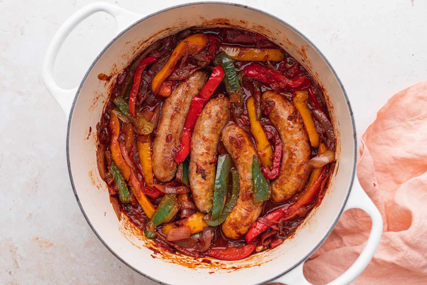 Overhead view of a dutch oven with polish sausage recipes with peppers and onions inside.