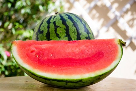 A quarter of a watermelon that's been cut lengthwise; a whole watermelon is in the background