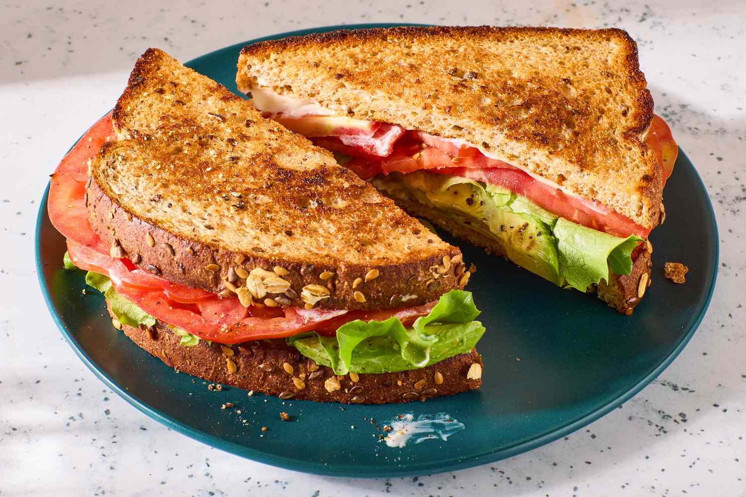 Avocado, lettuce, and tomato sandwich on whole grain bread, served on a teal plate