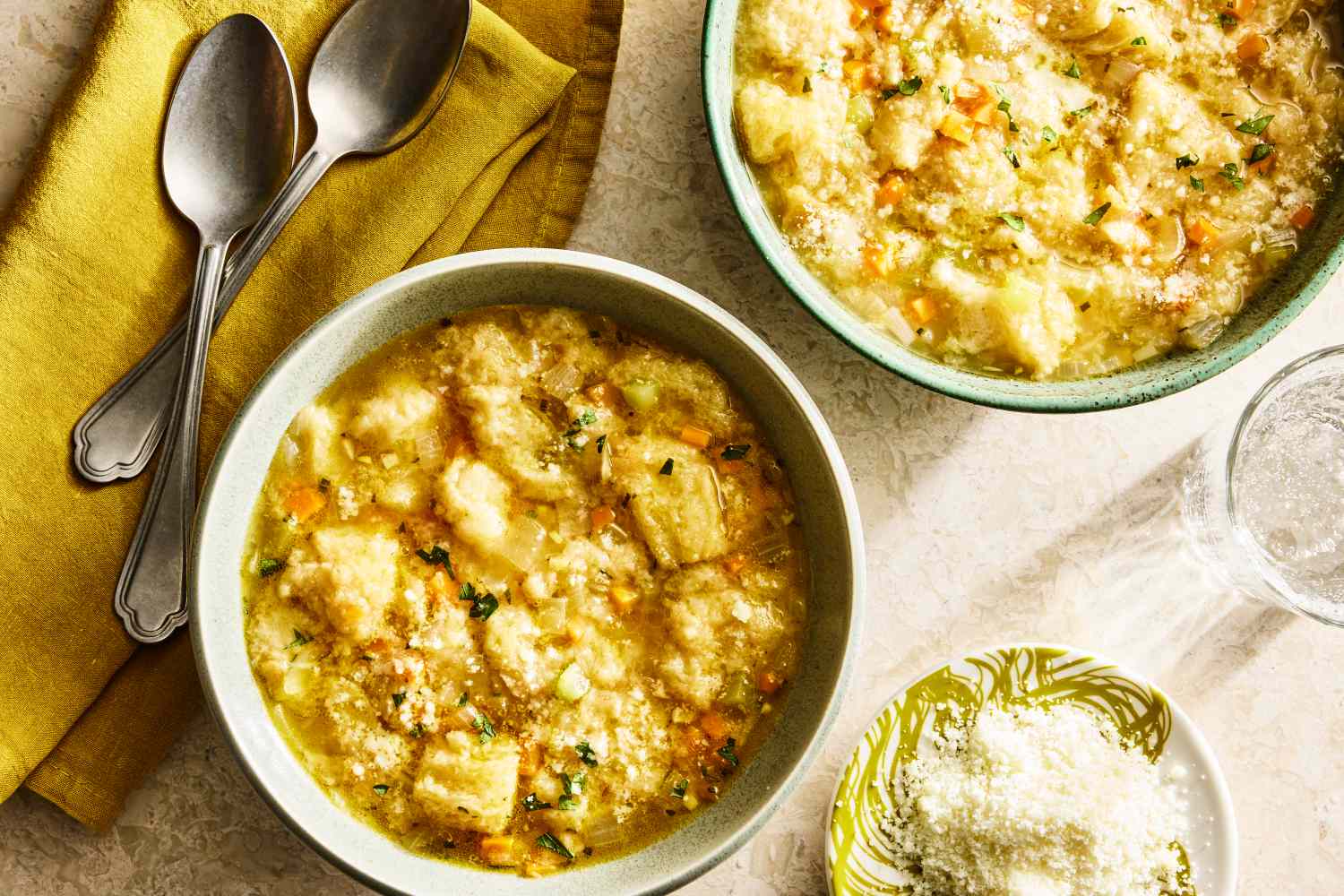 Bowls of pancotto soup with bread and vegetables accompanied by grated cheese and spoons