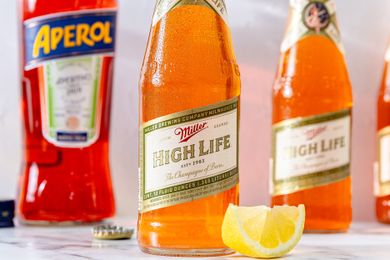 Miller High Life beer bottle with a lemon wedge Aperol bottle in the background