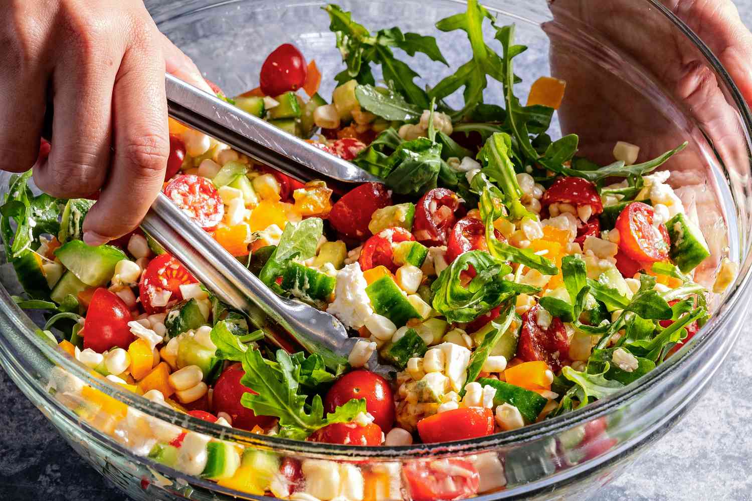 A salad being tossed together in a bowl with tongs