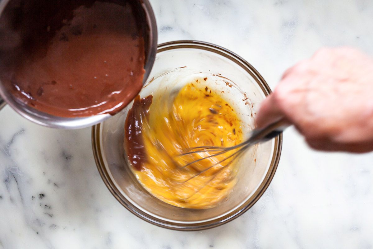 Whisking chocolate into a glass bowl to make a chocolate pudding recipe.