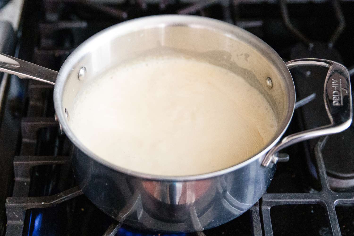 Angled view of a saucepan of butter, flour and evaporated milk simmering on a gas stovetop from Baked Mac and Cheese recipe