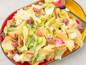 A plate of potato chip salad with grapes and apple slices on a yellow-red platter