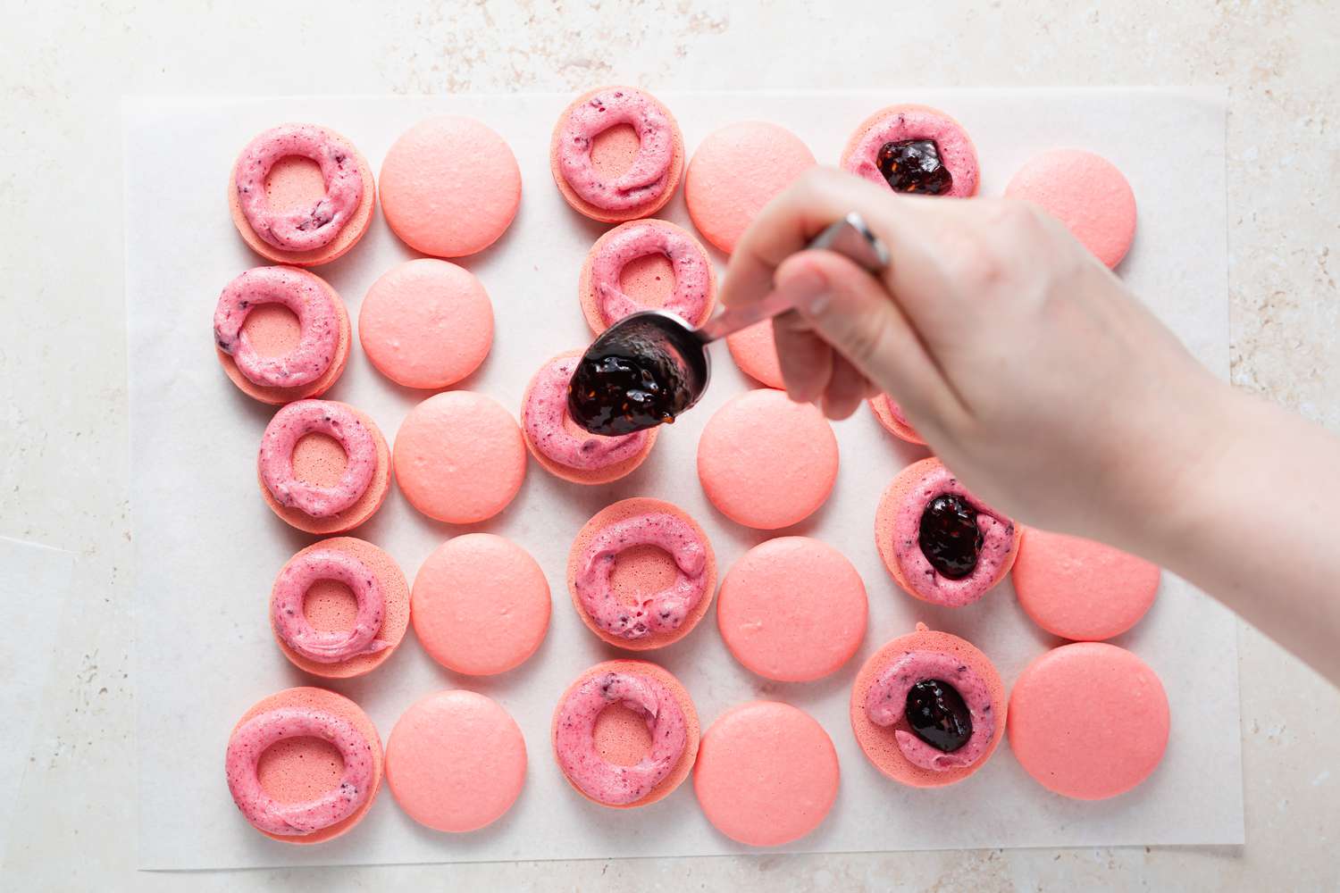 Spooning jam into the center of a buttercream lined macaron.