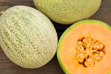 Whole cantaloupes and a cantaloupe half exposing seeds, placed on a textured surface