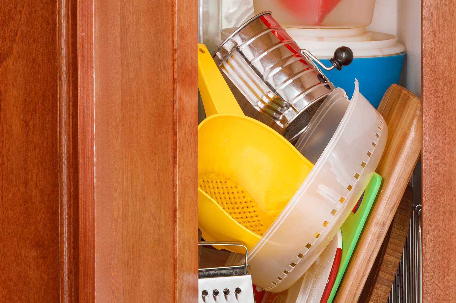 A messy and cluttered kitchen cabinet with a jumble of accessories and utensils