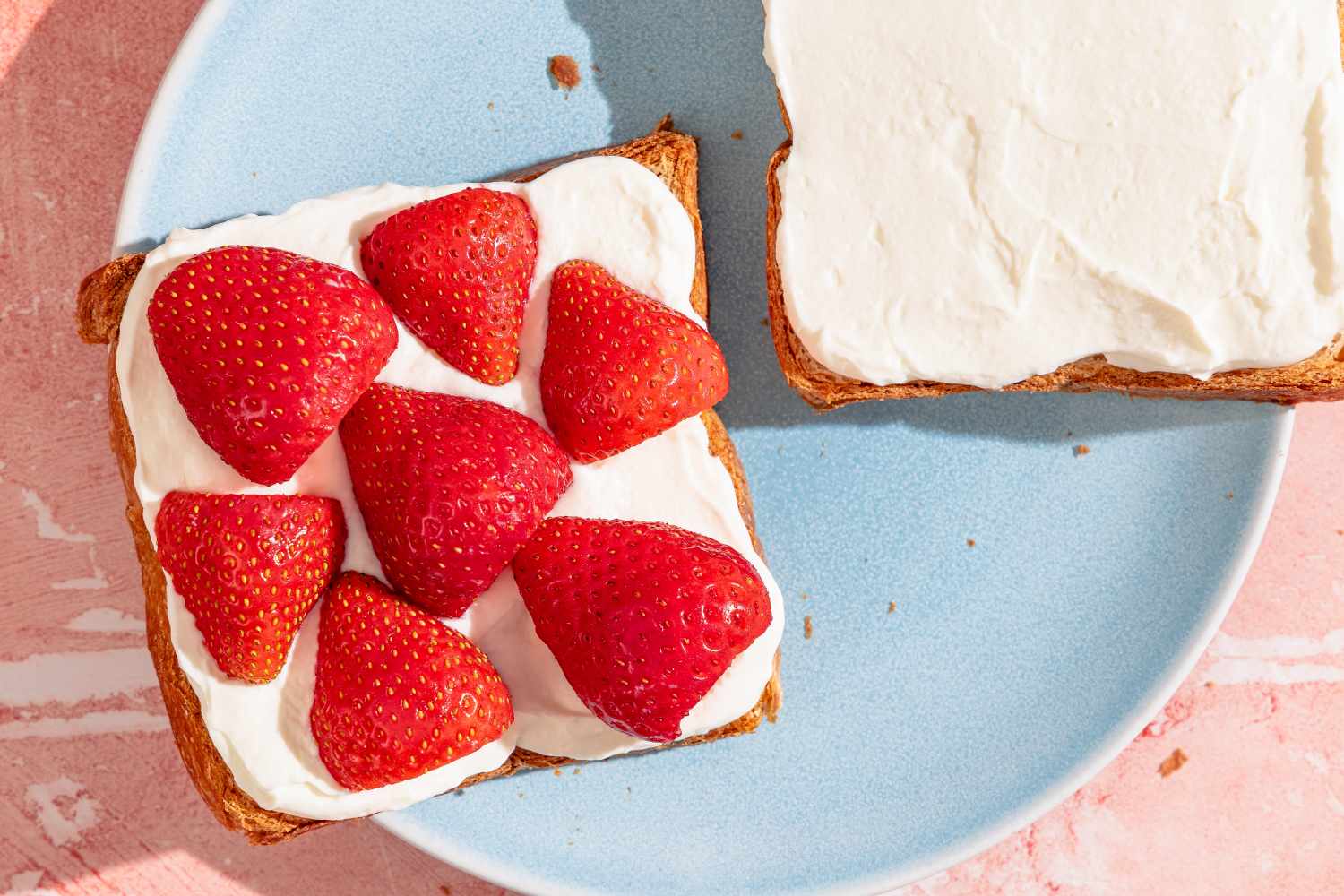 Two pieces of toast one topped with cream and strawberries on a plate