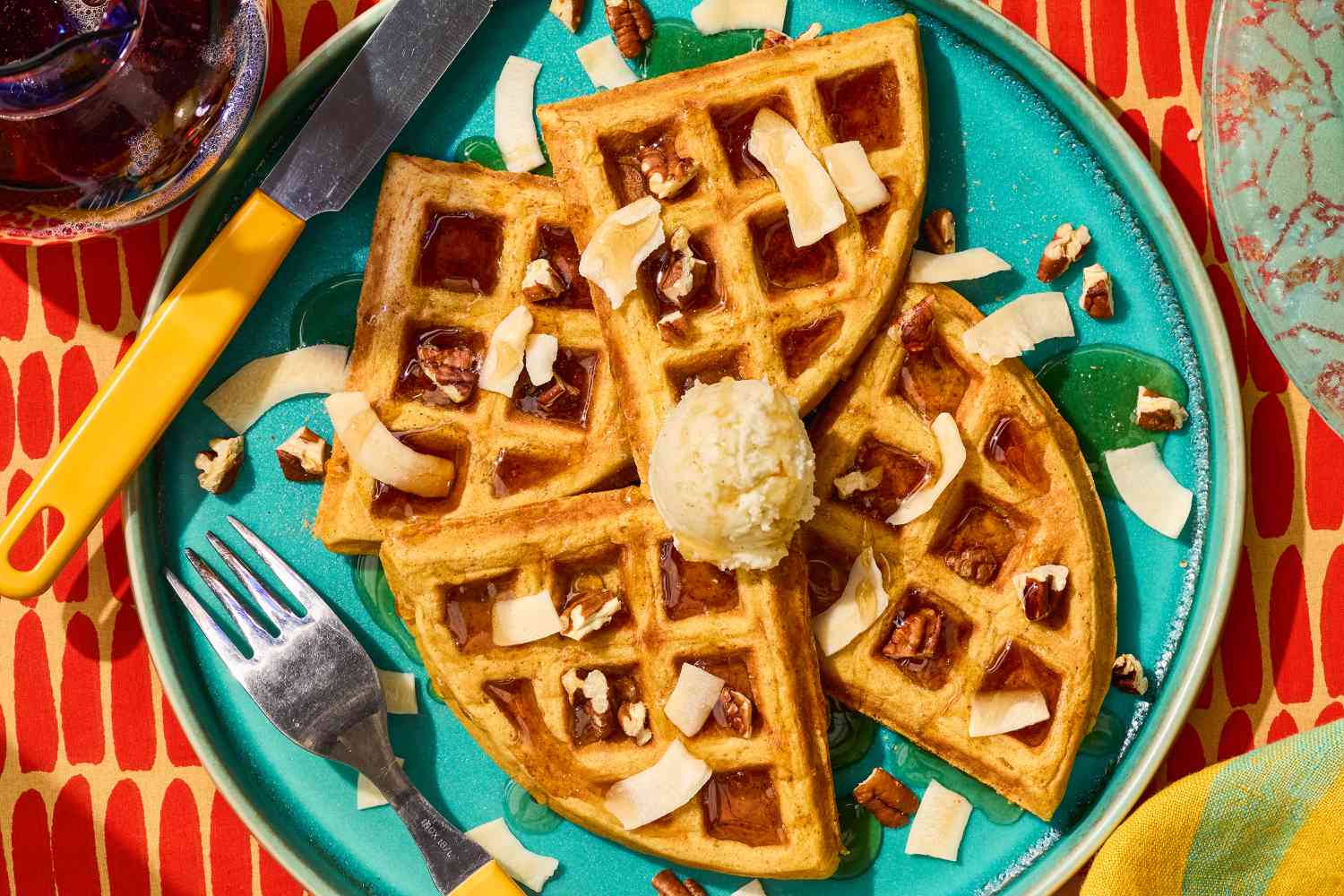 Plate of Carrot Cake Waffles, garnished with butter, syrup, chopped pecans, and toasted coconut flakes