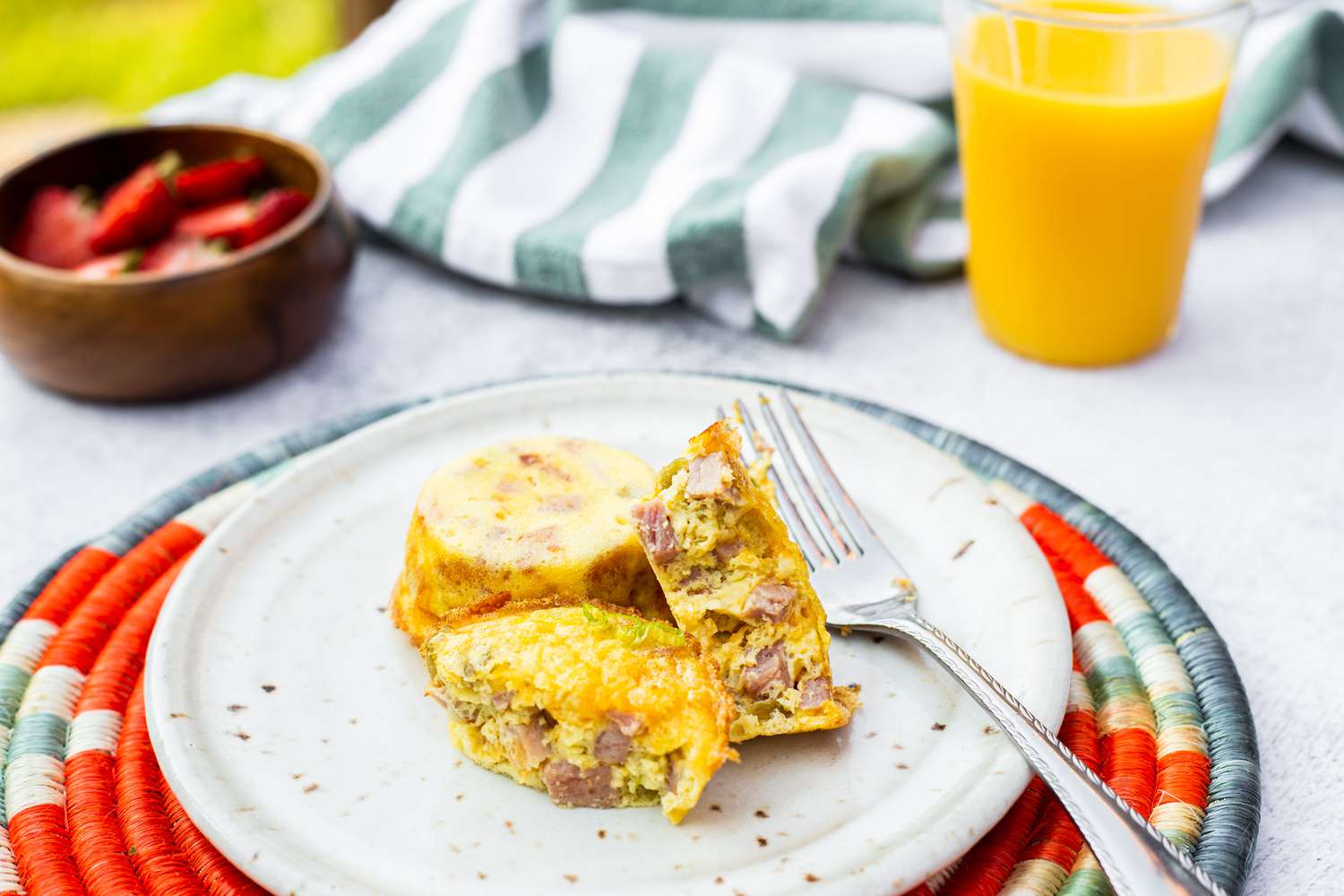 Ham, Cheddar, and Green Chile Egg Bites on a Plate Next to a Bowl of Strawberries and a Glass of Orange Juice