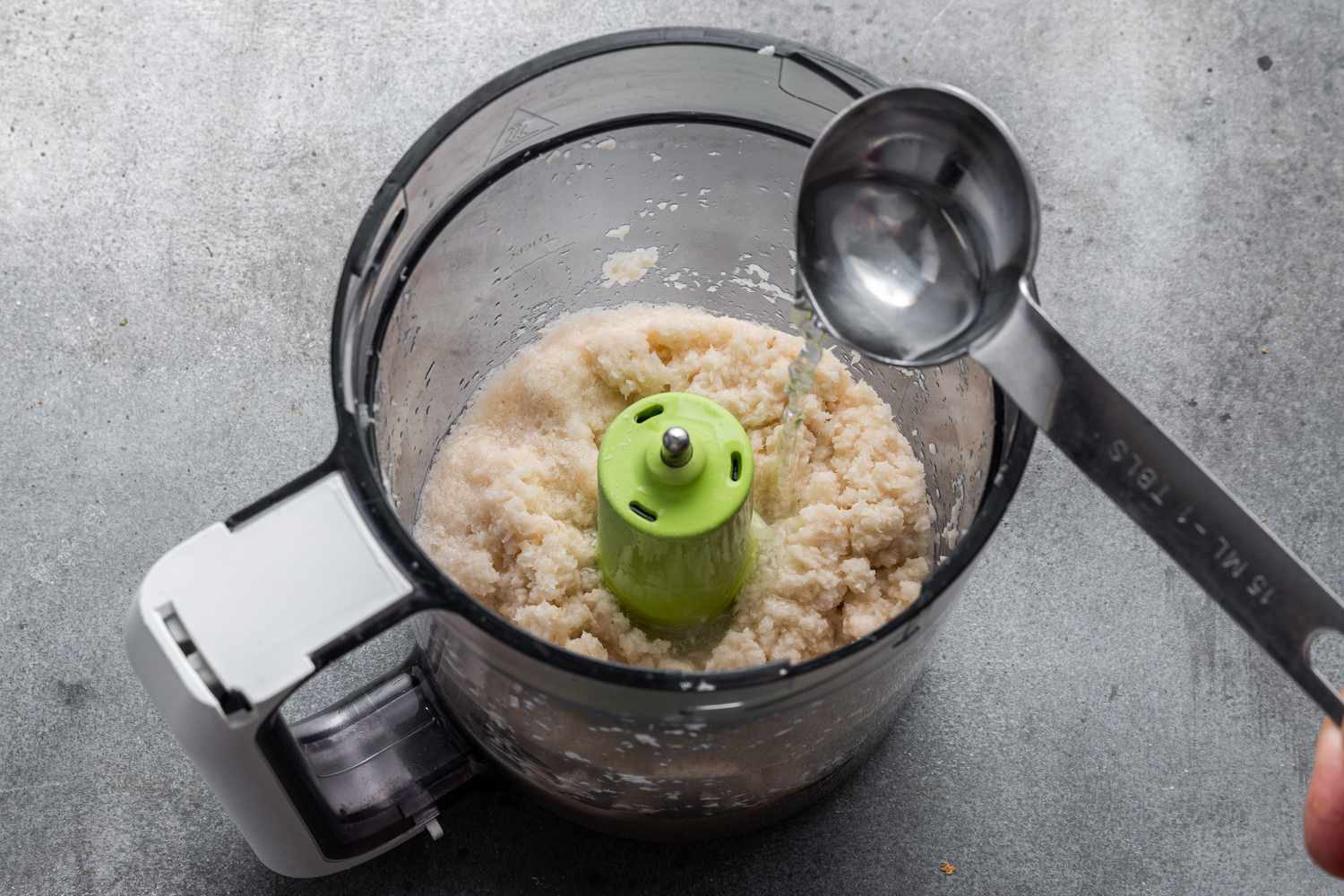 Adding vinegar to grated horseradish root in a food processor