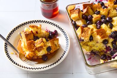 Plated serving of blueberry maple breakfast bake, drenched in maple syrup, alongside baking dish of the bake