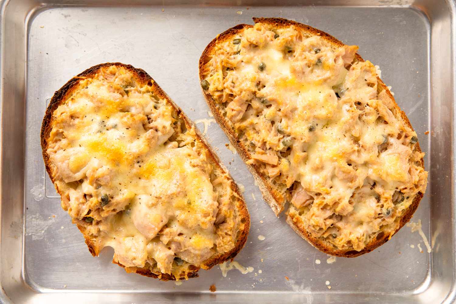 Two toasted bread slices topped with a cheesy tuna mixture on a baking sheet