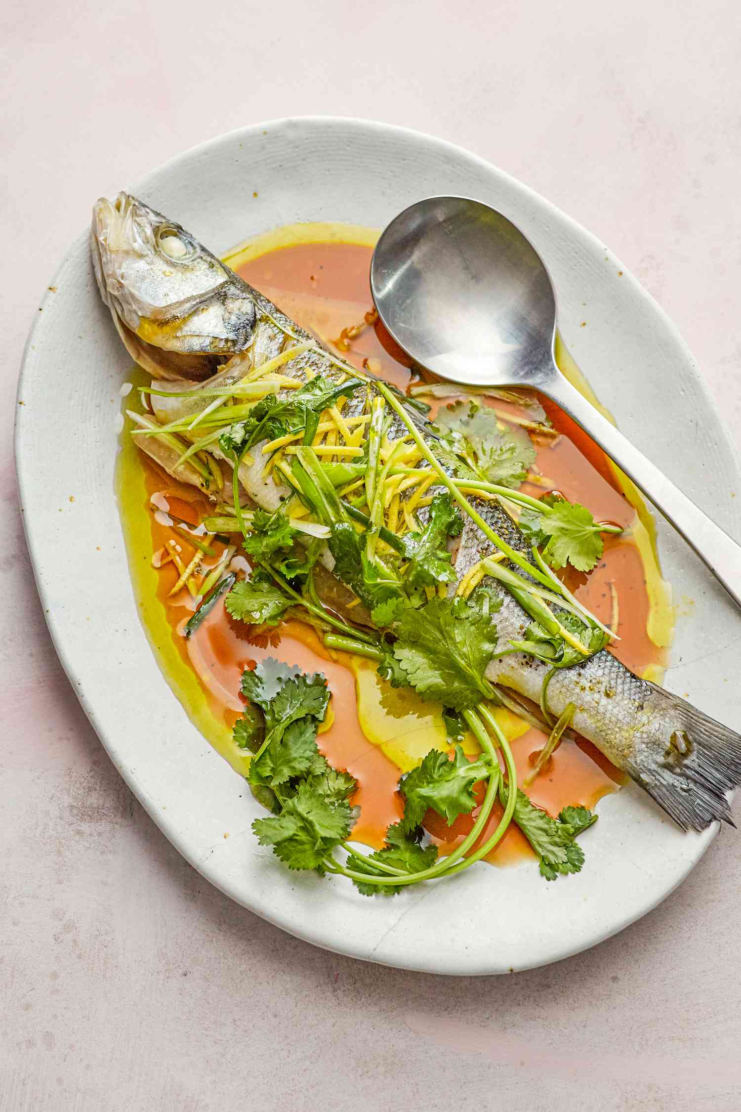 Overhead view of a steamed whole fish on a flatter and topped with sauce and herbs.