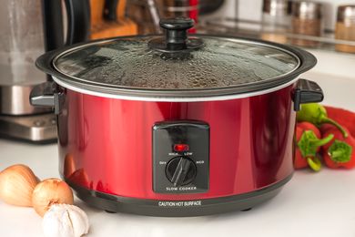 A slow cooker with vegetables and garlic on a countertop