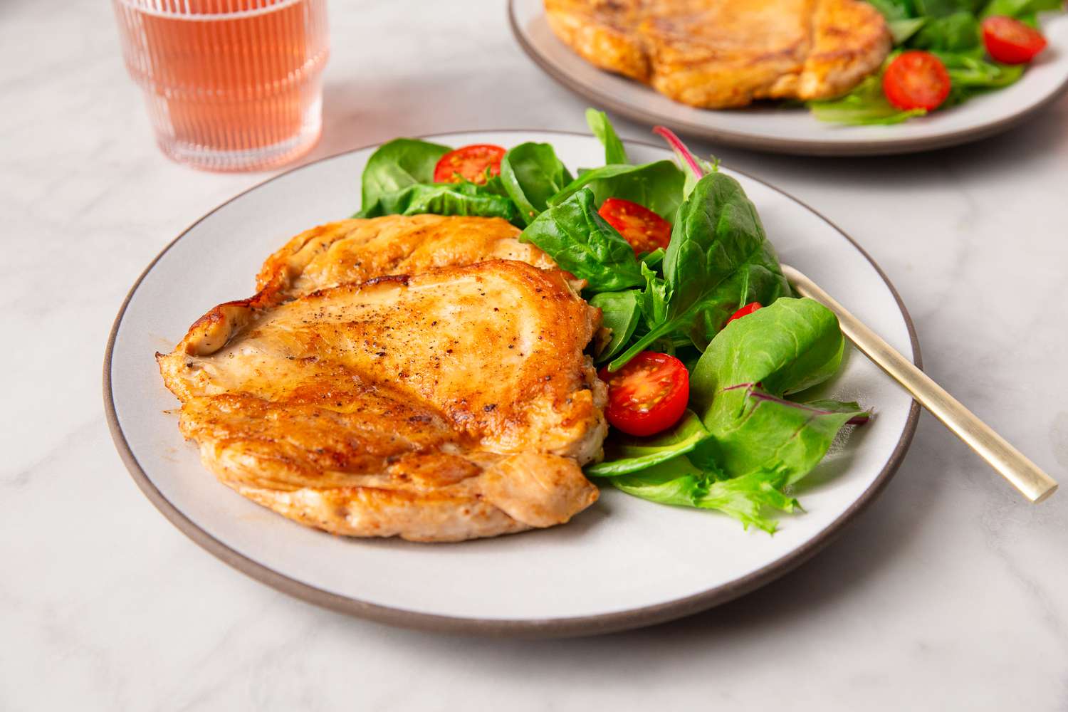 A plated dish consisting of cooked chicken and a salad with greens and cherry tomatoes, served on a table