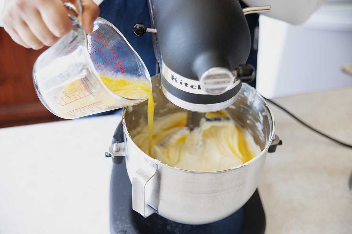 Woman adding eggs to creamcheese to make creme brulee cheesecake batter