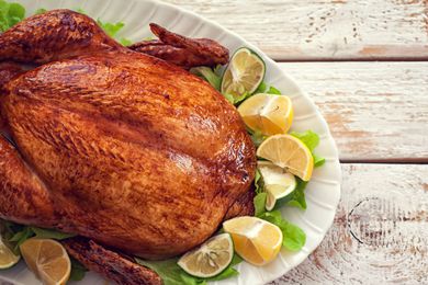 A roasted turkey on a white serving platter, garnished with lemon wedges and lettuce leaves