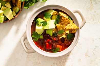 Bowl of tortilla soup with avocados chips and cilantro garnishes